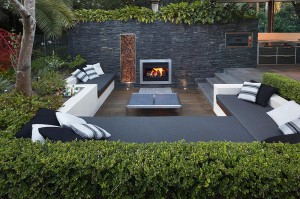 Outdoor-Living-with-Sunken-Lounge-lit-fireplace-in-stone-wall-with-hedging